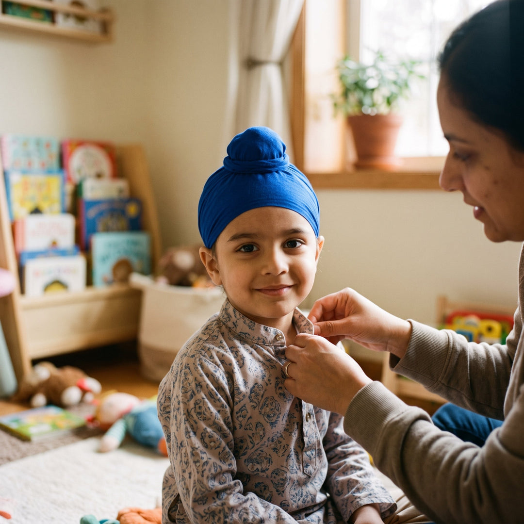 A smiling child wearing a blue patka sits while an adult gently adjusts the collar of their patterned shirt in a cozy, toy-filled room.